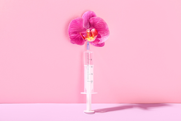 Medical Syringe With an Orchid Flower On a Pink Background